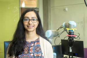 Gopika Ajaykumar poses in front of a robot arm.