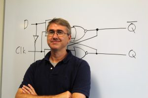 David Hovemeyer poses in front of a whiteboard with electrical symbols written on it.