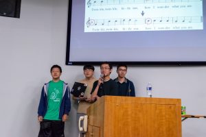 The team members of Noteshift present their work in Hodson 110. Music notes and the lyrics of "Twinkle Twinkle Little Star" are displayed on the projector screen behind them.