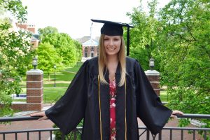 Katarine Mayer in graduation garb posing in front of Wyman Quad.