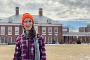 Sabrina Mielke, wearing a bright orange hat, poses on Decker Quad in front of Mason Hall.