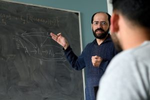 Professor Ilya Shpitser gestures to a blackboard in front of a student.