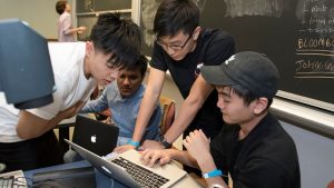 A group of students huddle around a laptop.