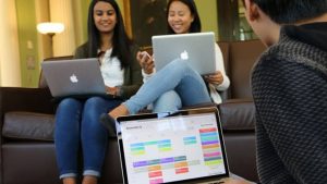 Three students converse while on their laptops. One screen displays a Semester.ly schedule page.