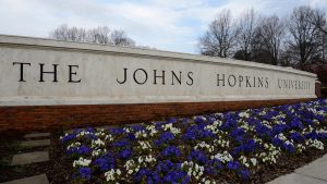 The Johns Hopkins University sign. Blue and white flowers are planted in front of it.