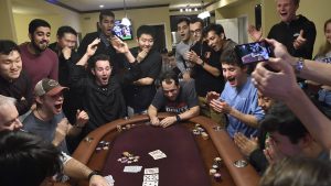 A group of students and faculty gather around a poker table, cheering with excitement.