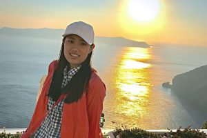Sally Hao poses in front of the sunset over an ocean with islands.