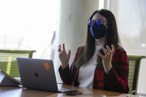 Yana Safonova wears a mask and gestures in front of her laptop in a conference room.