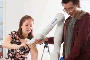 Two students adjust a robot arm.