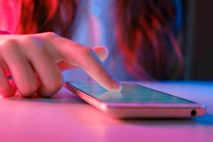 A woman puts a finger on a smartphone placed on a flat surface.