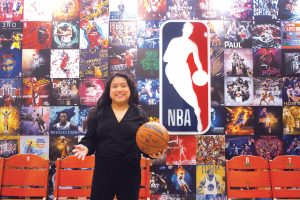 Paige Senal poses with a basketball in front of the NBA logo.