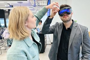 A woman helps a man adjust a VR headset.