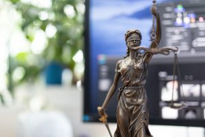 Bronze statue of a woman with scales as the symbol of law and justice in front of a computer monitor and potted plant.