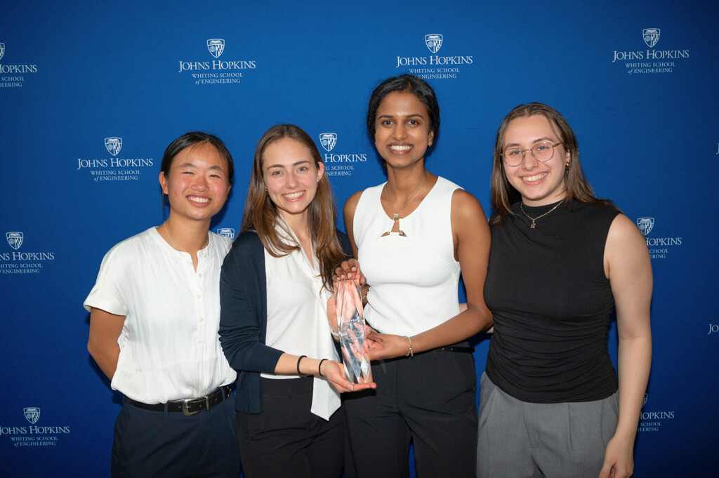 The TriageNow team poses with a trophy in front of a Johns Hopkins background.