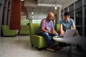 Professor Sanjeev Khudanpur sits beside PhD student Drew Prinster and looks at his laptop.