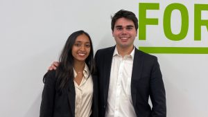 Iris Gupta and Charlie Wheelock pose in front of a white wall with green text.