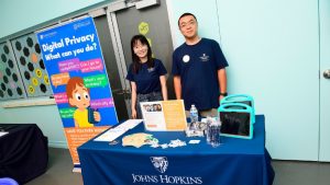 Lanjing Liu and Yaxing Yao pose behind a table reading Johns Hopkins Whiting School of Engineering Department of Computer Science and in front of a banner reading Digital Privacy What can you do?
