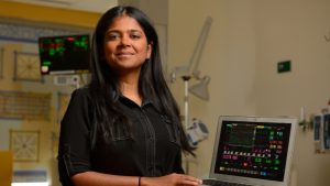Suchi Saria poses with a laptop displaying the TREWS dashboard.