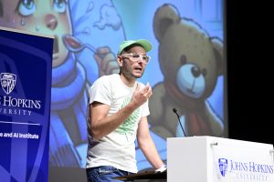 Mathias Unberath speaks on stage behind a podium in front of a screen displaying an illustration of a sick child holding a teddy bear.