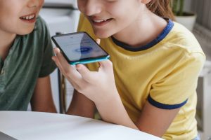 Two children speak to a chatbot on a cellphone.