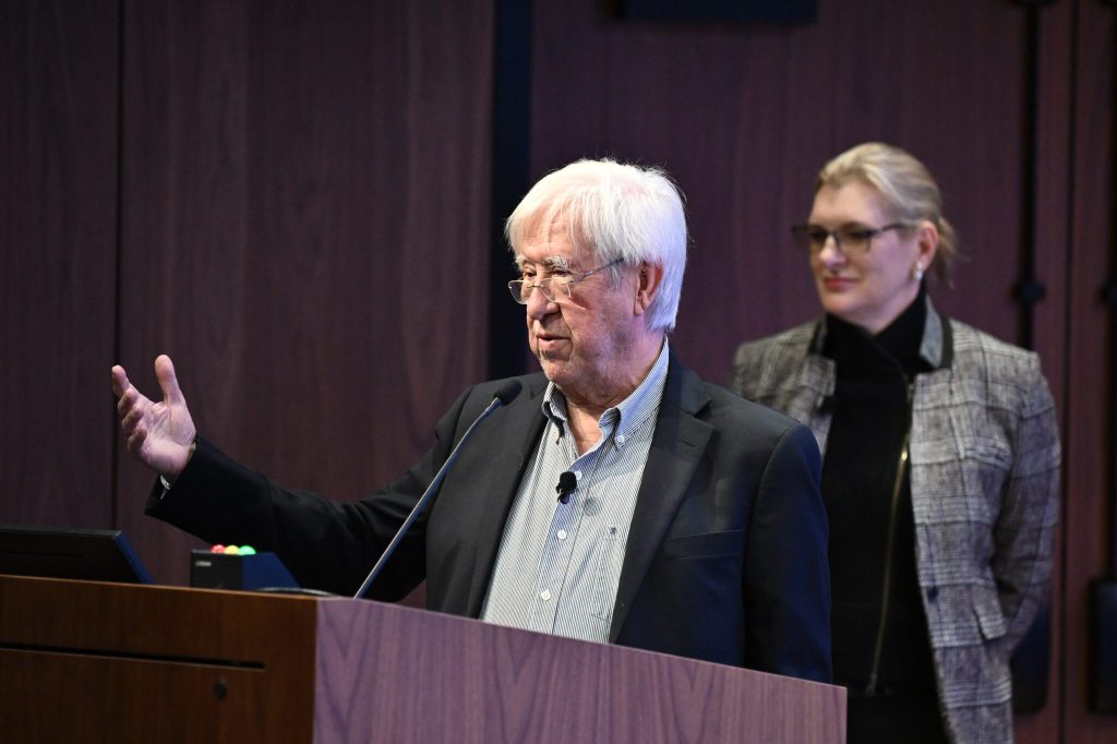 Alex Szalay speaks at a lectern with Janis Taube looking on.