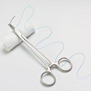 Needle holder put on white bandage as suture set.