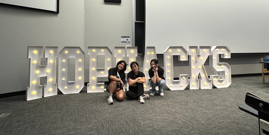 Three organizers sit in front of large, light-up HOPHACKS letters.