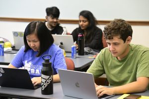 A variety of students hunch over their laptops with concentrated expressions.