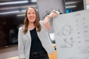 Alexis Battle standing with her arm propped on a whiteboard with equations and figures written on it.