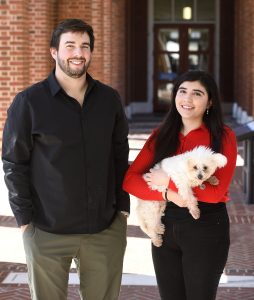 Eric Nalisnick stands next to Alessa Carbo, holding her small white dog Frida, in the breezeway between Malone and Mason Halls.
