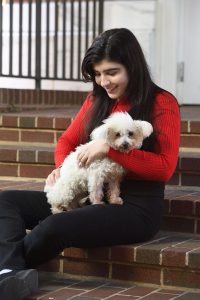 Alessa Carbo sits on brick steps holding her small white dog, Frida.