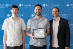 Michael Rushanan poses with his awards and two students.