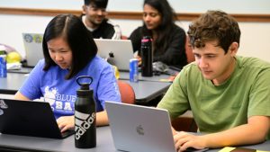 A variety of students hunch over their laptops with concentrated expressions.