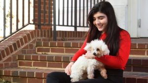 Alessa Carbo sits on brick steps holding her small white dog, Frida.