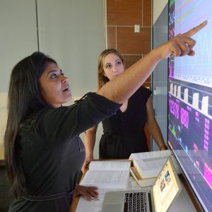 Suchi Saria and another researcher look at figures and graphs on a large computer screen.
