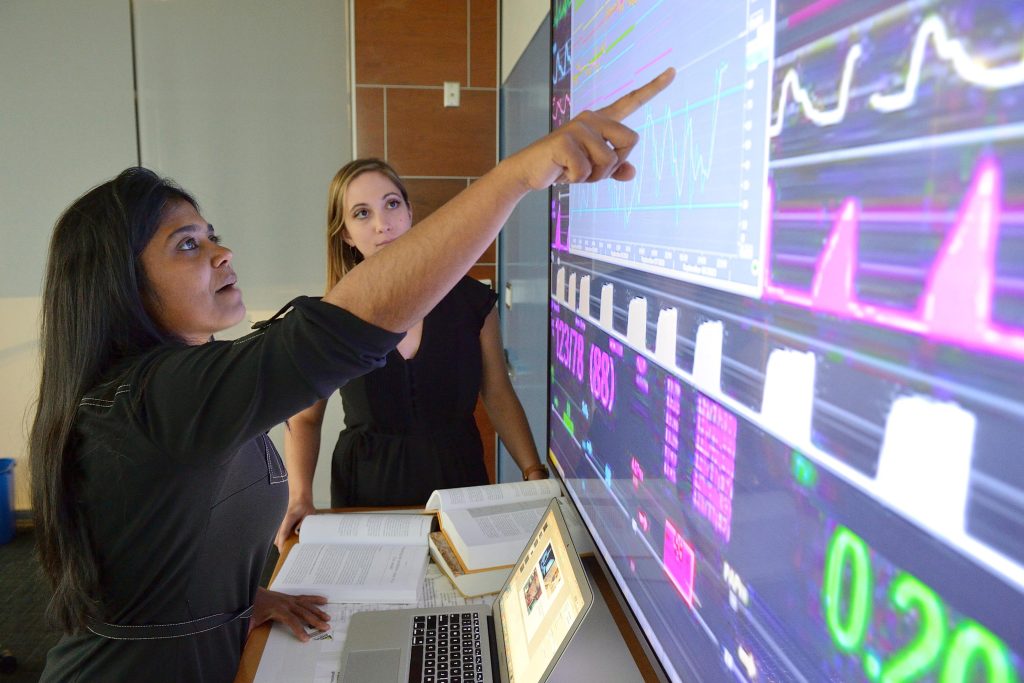 Suchi Saria and another researcher look at figures and graphs on a large computer screen.