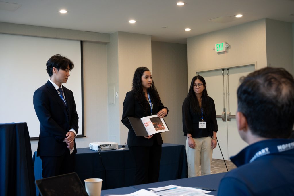 Gabrielle Chavez holds a photo album while Kurtis Yoon and Katie Cariaga look on in front of a panel of judges.
