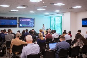 Chien-Ming Huang presents "Conversational Agents for Behavioral Medicine" on TV screens in front of the audience at the in-person convening of the Johns Hopkins Workgroup on AI and Healthcare.