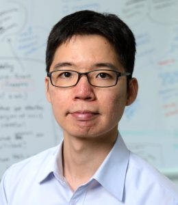Headshot of Chien-Ming Huang in front of a whiteboard covered in equations.
