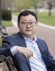Headshot of Tianmin Shu sitting on a bench on the Homewood campus.