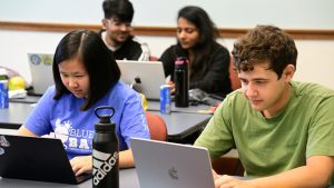 A variety of students hunch over their laptops with concentrated expressions.