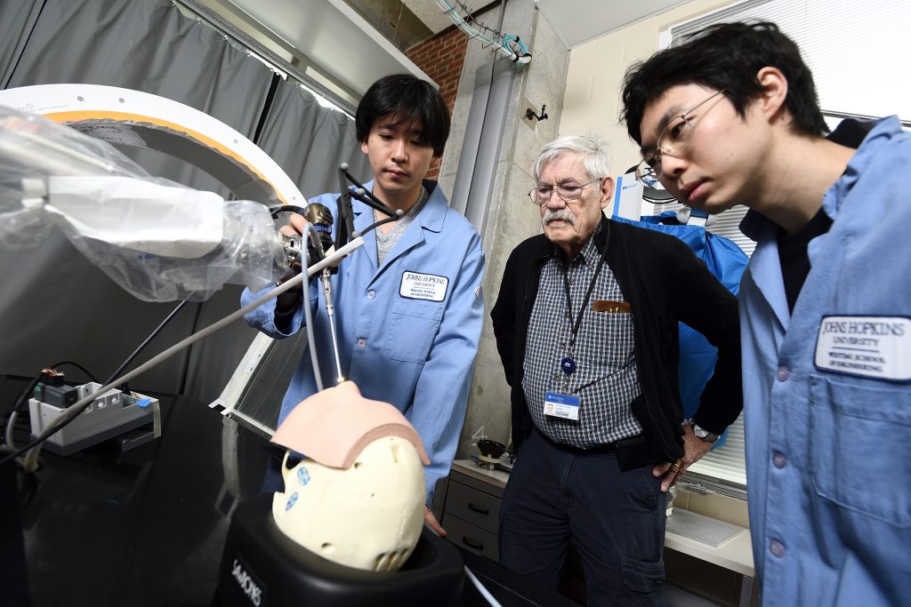 Russell Taylor and students lean over a robotic device operating on a phantom skull in the Mock OR.